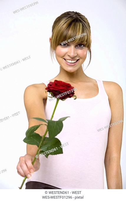 Young woman holding red rose, smiling, portrait, close-up