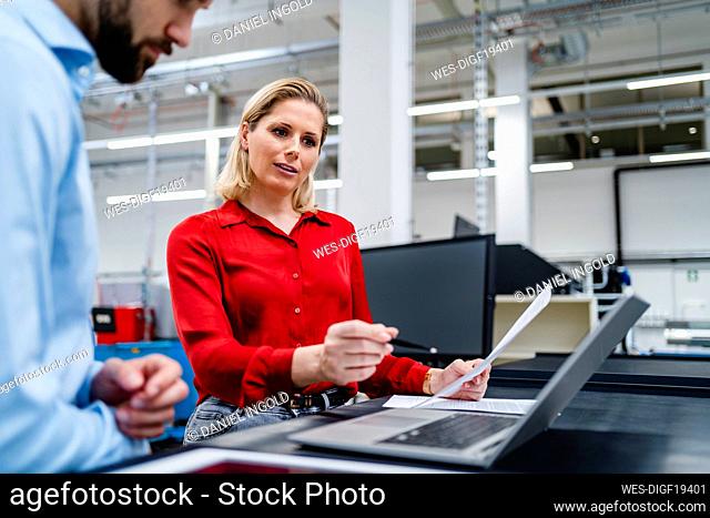 Businesswoman discussing with colleague over laptop at factory