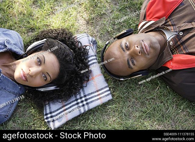 African couple listening to headphones in grass