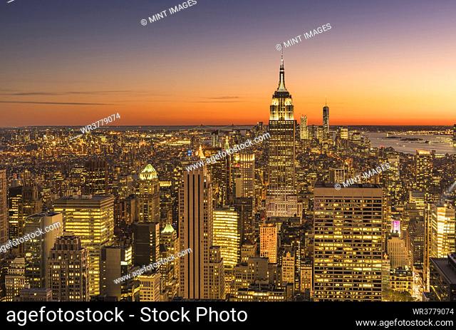 Empire state building rising above Manhattan skyline at sunrise or sunset