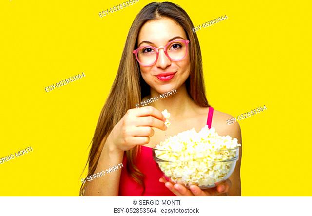 Girl with positive emotion holding pop corn and watching comedy movie isolated on yellow background studio portrait