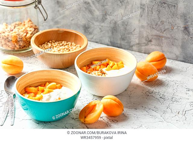 Natural yoghurt with pieces of apricots, granola and pine nuts in two bowls on light background