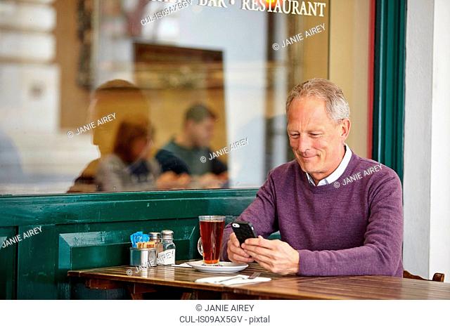 Mature man reading smartphone text at sidewalk cafe table