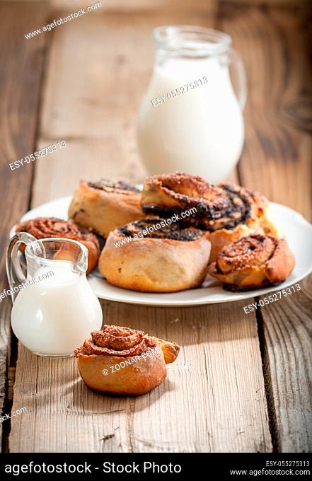 Cinnamon rolls and Bun with poppy seeds on a plate and small jugs of milk