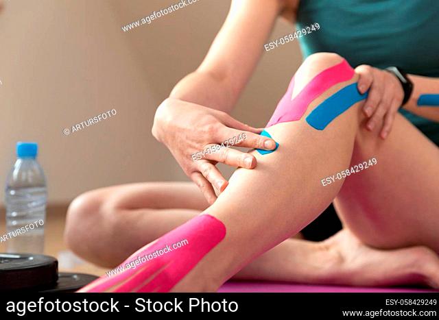 Young fit women applying elastic kinesiology tape on her knee. Muscle treatment, rehabilitation sport and physical therapy. Workout at home