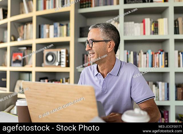 Happy mature businessman sitting in front of bookshelf
