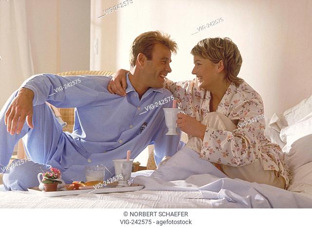 portrait, indoor, full-figure, young blond couple wearing pyjama sit on a Sunday morning at breakfast in bed  - GERMANY, 07/03/2005