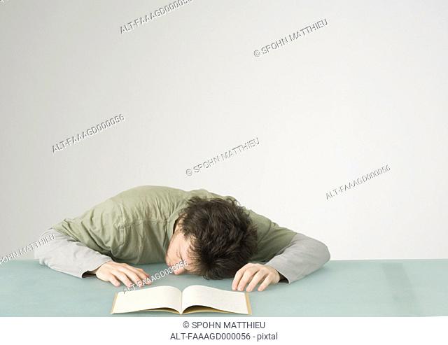 Young man with head on table in front of open notebook