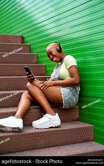 Cheerful woman text messaging through smart phone while sitting on steps