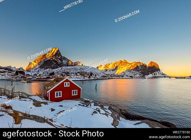 Renovated rorbu fishing hut on rocky coast on the Lofoten islands in Norway in winter with ocean and snow capped mountains