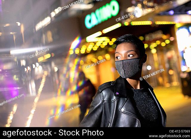 Young woman in studded face mask on city street at night