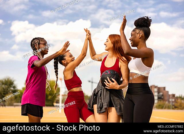 Happy multiracial friends doing high five in sports court
