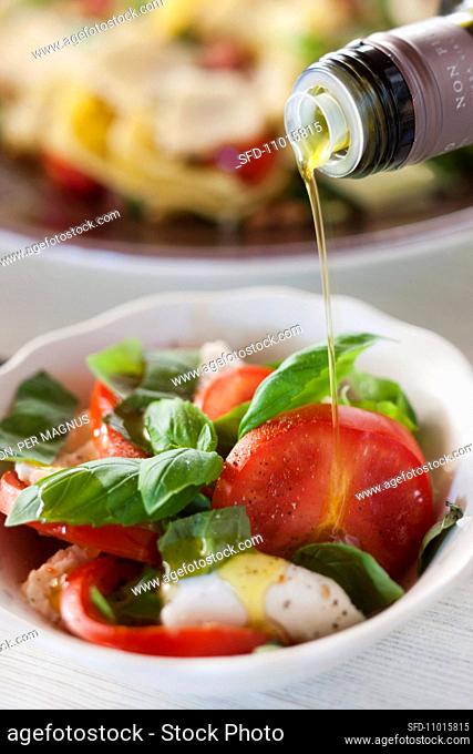 Sprinkling insalata caprese with olive oil