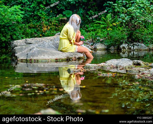 Attractive blonde woman on a Green forest river with bunch of flowers in hand