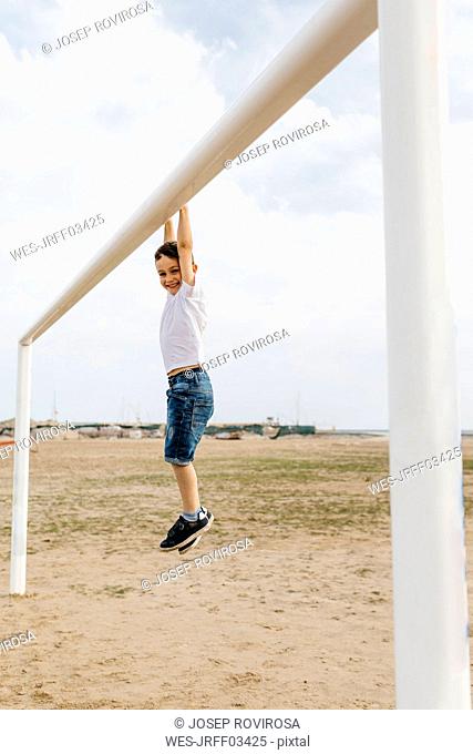 Boy hanging from the goal on the beach