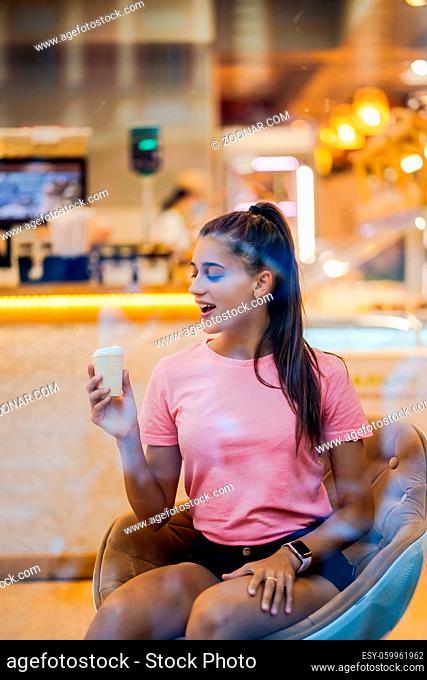 Smiling girl eating an ice-cream in a waffle cup in a cafe