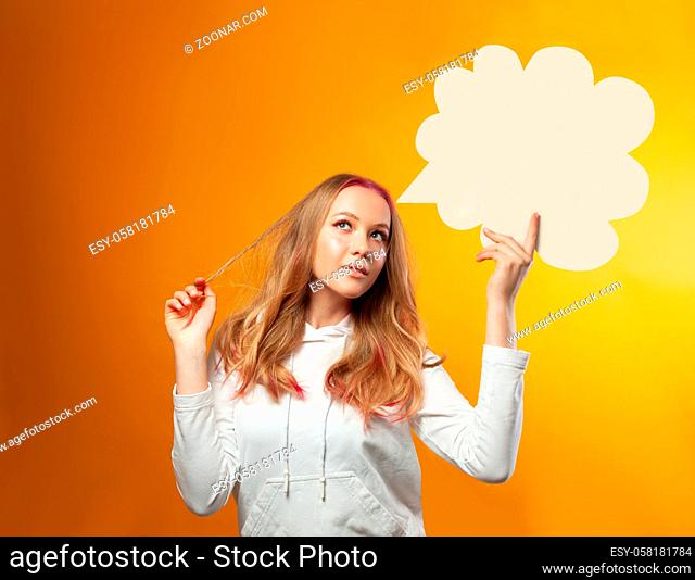 The pensive young woman stands on a yellow background. She holds a cloud with copy space. The concept of woman thoughts