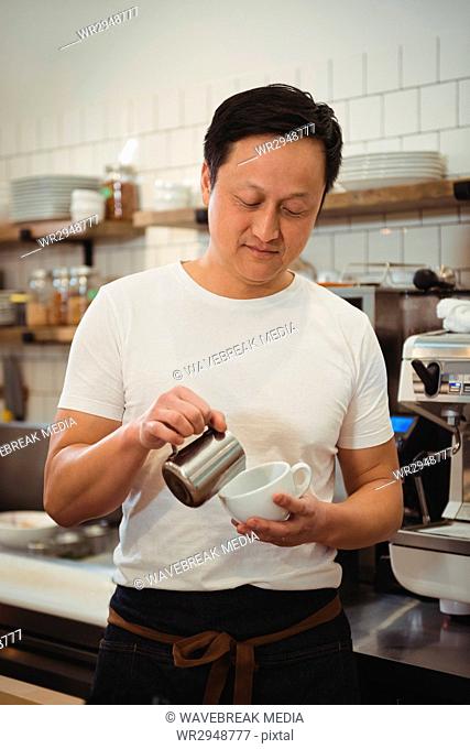 Barista pouring milk into coffee cup at cafe