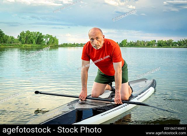 Environmental portrait of a senior paddler on his stand up paddleboard on a calm lake in Colorado