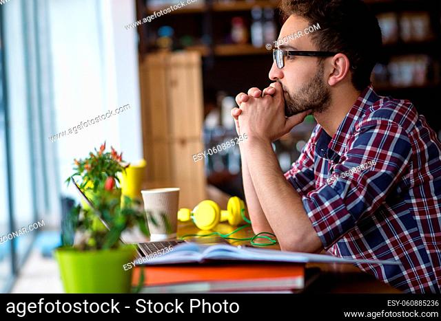 Profile of serious handsome freelance man in glasses working in restaurant or cafe. Man looking at window and thinking about something