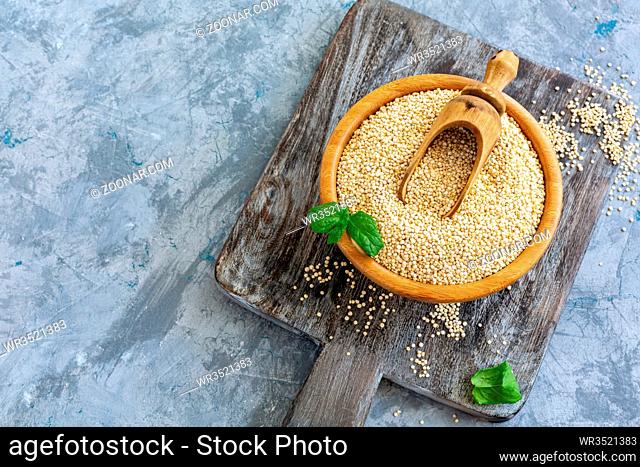 Raw quinoa seeds and wooden scoop in bowl on serving board on textured concrete background. Top view