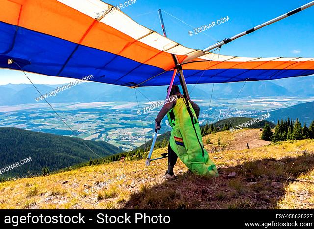 Hang glider preparing to take off from mountain top hill. Kootenay valley mountains in background, Creston, British Columbia, Canada. View from behind