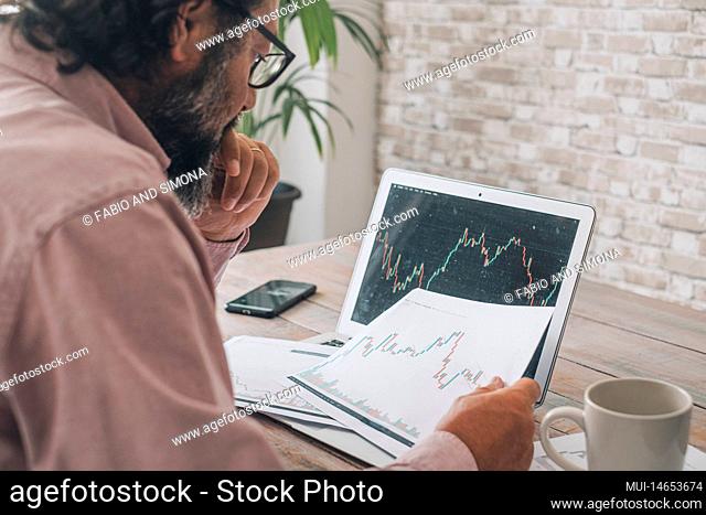 One man looking and studying stock market charts at the desk with opened laptop and connection. Concept of economy crypto forex exchange business job