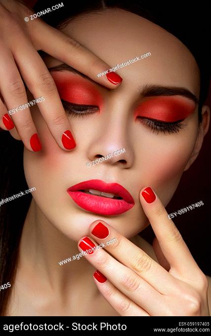 Closeup portrait of beautiful young woman with bright red eyeshadows, lips and nails