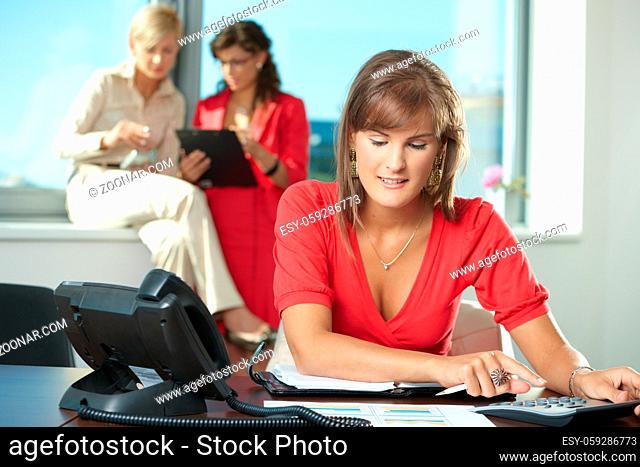 Young businesswoman sitting at office desk, using digital calculator, smiling