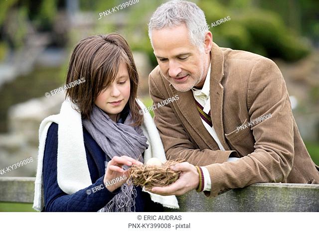 Man with his daughter holding a bird's nest in a park