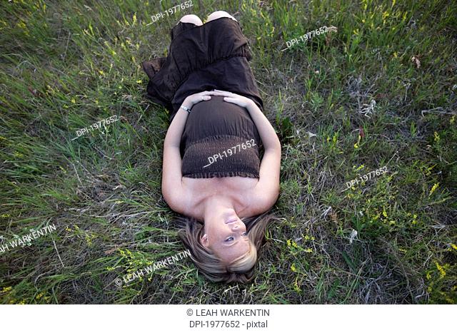 a pregnant woman lays on her back on the grass, edmonton alberta canada