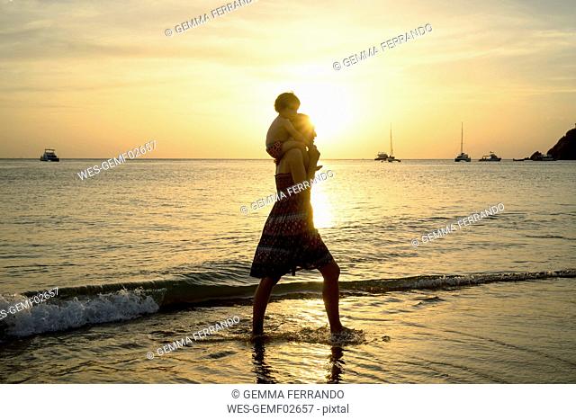Thailand, Koh Lanta, silhouette of mother with baby girl on her shoulders at seashore during sunset