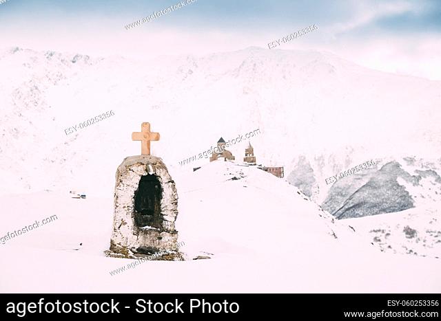 Stepantsminda, Gergeti, Georgia. Cross On Stones On Mountains Background Near Gergeti Trinity Tsminda Sameba Church In Snowy Winter Day