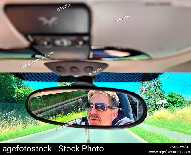 Reflection of senior mans eyes in rearview mirror of car with wet windshield