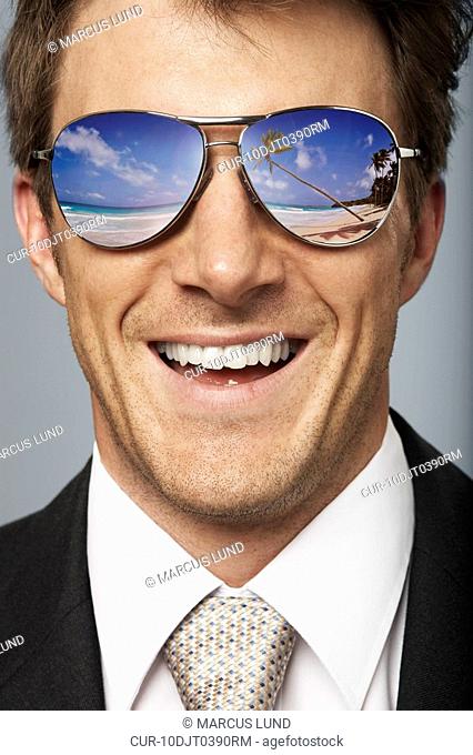 Smiling business man wearing sunglasses with reflection of a tropical island
