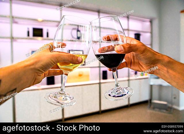 white and red wine glasses cheering selective focus, white interior design of modern bottles display shelves, winery cellar tasting room background