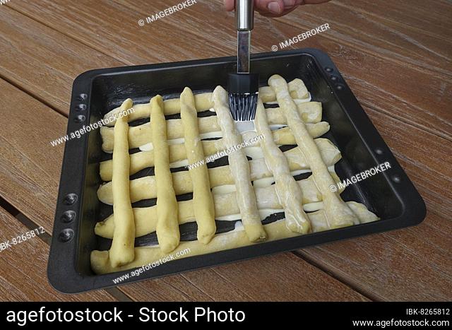 Swabian cuisine, preparing Bruckhölzer, Schlanganger, Sperrknechte made from potato dough, spreading dough rolls on baking tray with cream, brush, man's hand