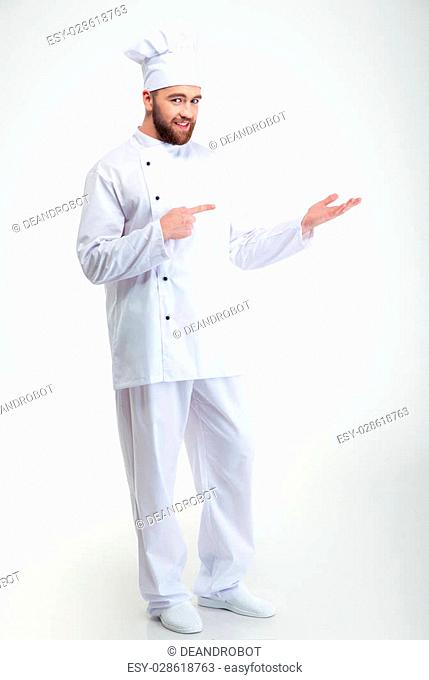 Full length portrait of a happy chef cook holding copyspace on the palm and pointing finger on it isolated on a white background