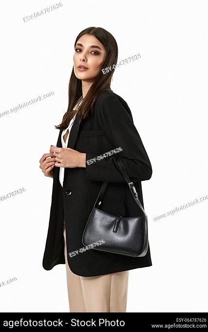 beautiful woman with black leather handbag in black blazer and beige pants isolated on white background