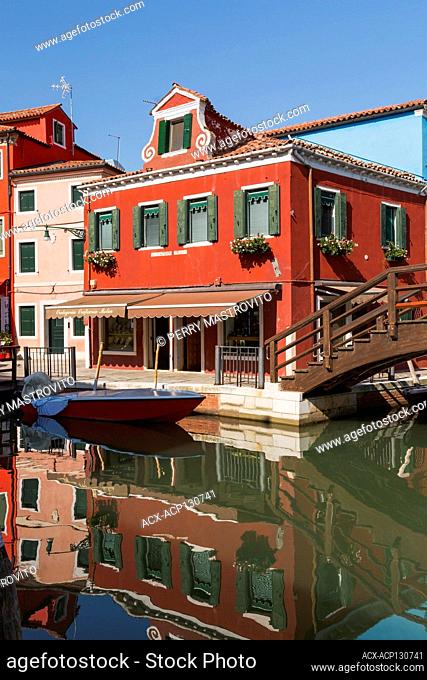 Brown wooden footbridge over canal with moored boat and pink and red stucco houses and a storefront, Burano Island, Venetian Lagoon, Venice, Veneto, Italy