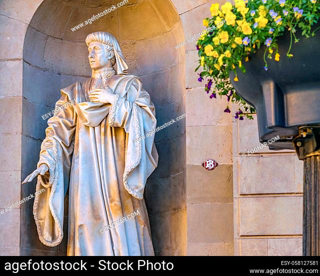 Stone sculpture of religious man with cassock at exterior niche of old building at gothic district in barcelona city, spain