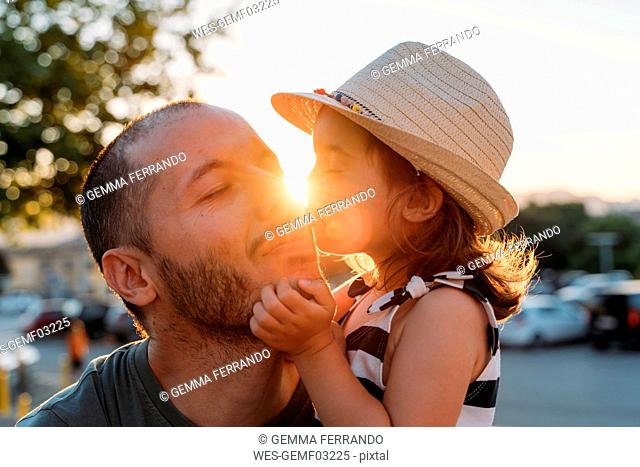 Little girl kissing her father at sunset