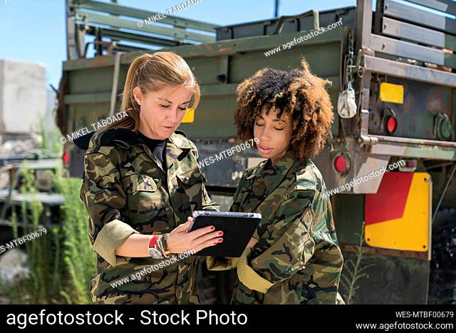 Female military soldiers discussing over digital tablet against truck on sunny day