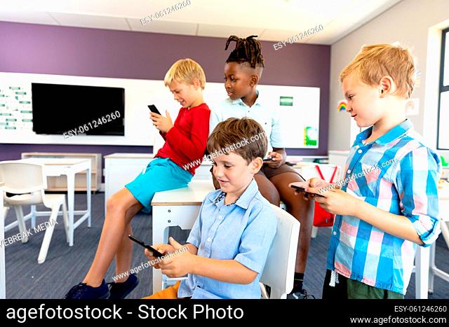 Multiracial elementary schoolboys using smart phone in classroom during school breaktime