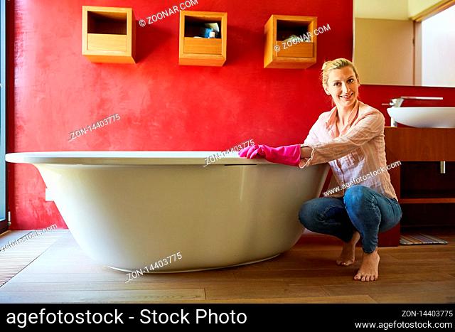 Lächelnde Putzfrau im Badezimmer beim reinigen der Badewanne beim Hausputz