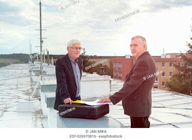 Two senior businessmen with documents making a business deal outdoors on the roof of a building