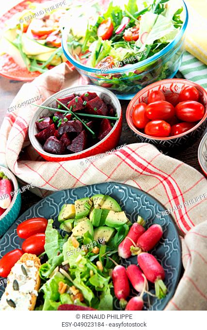 bowls and plate of healthy vegan salad . Various vegetables avocado, cucumber, radishes on the wooden background