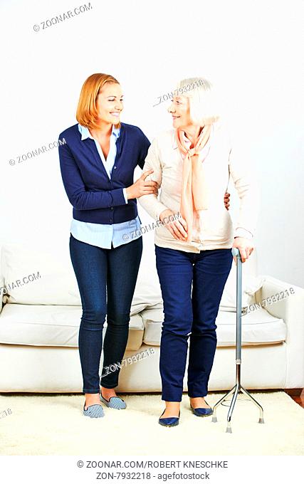 Frau als Altenpfleger hilft einer Seniorin mit Gehstock zu Hause