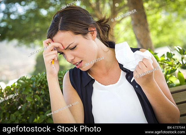 Frustrated and upset young woman with pencil and crumpled paper in her hand sitting on bench outside
