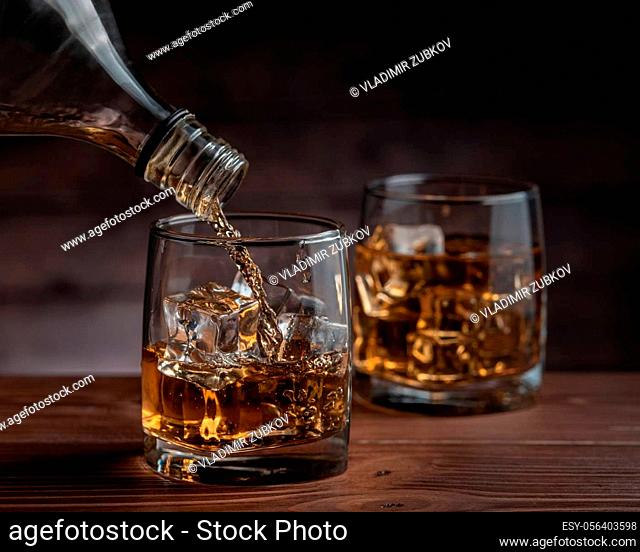 Two glasses of whiskey on the rocks, one filled with whiskey from a bottle, close-up